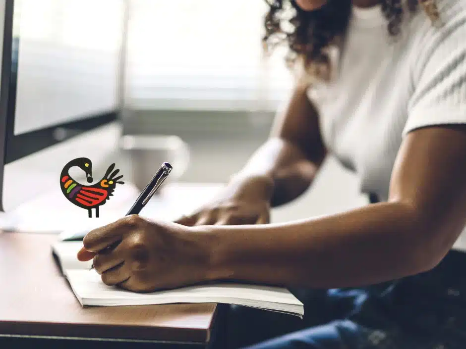 A Black woman writes in a notebook. A Sankofa bird illustration is by her hand.