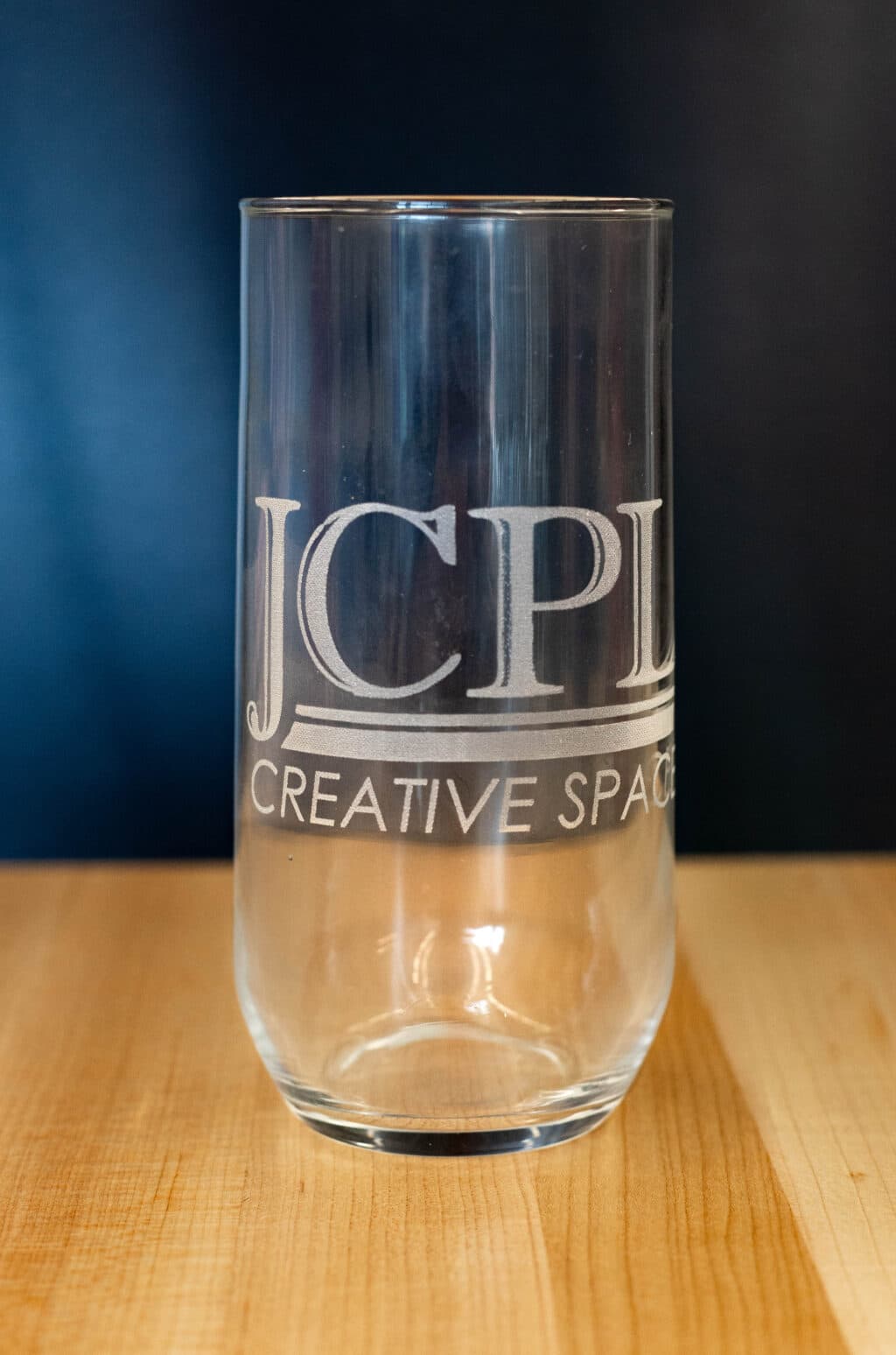 Drinking glass with JCPL Creative Space etched on it.