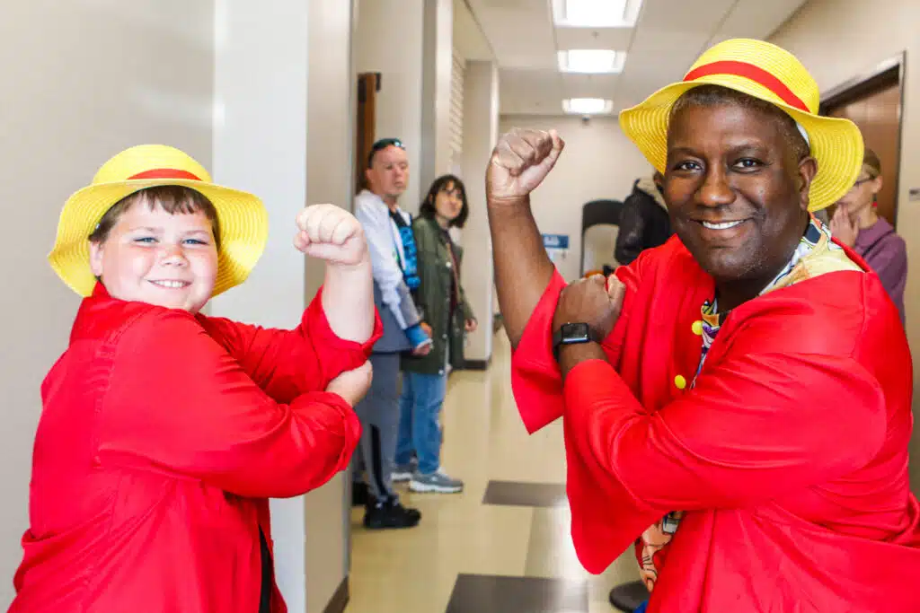 A boy and a man both pose as Luffy from One Punch Man.