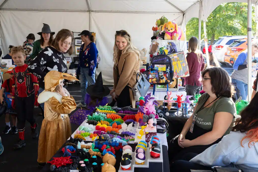 A child and two adults visit a vendor's colorful booth.