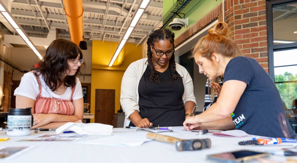 A library staff person teaches two women how to make jewelry in the Creative Space.