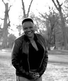 Author photo of LeTonia Jones, an African American woman with short hair. She is standing outside in front of some bare trees. She is smiling and wearing a black leather jacket.