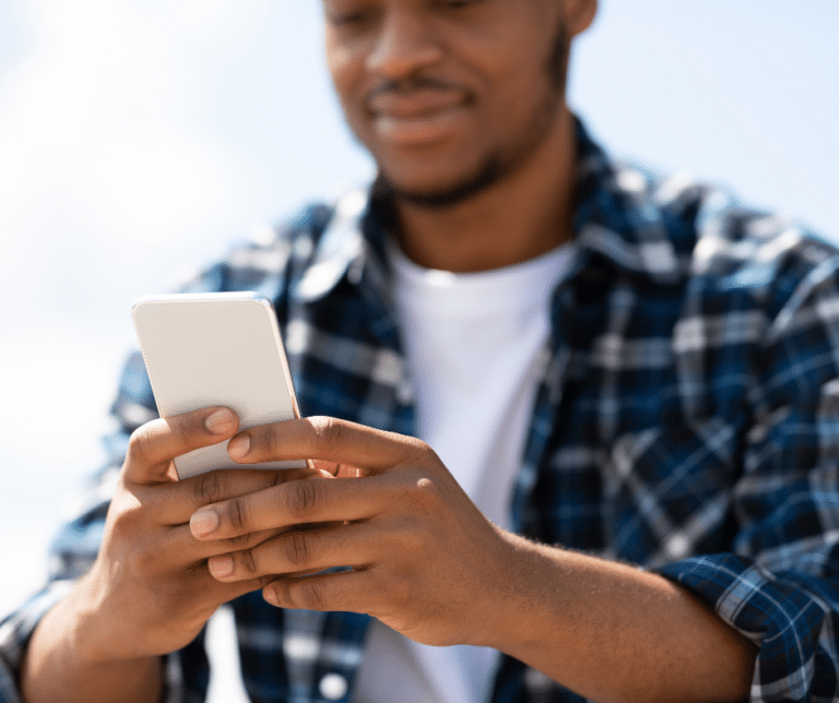 A young Black man is smiling while using his phone
