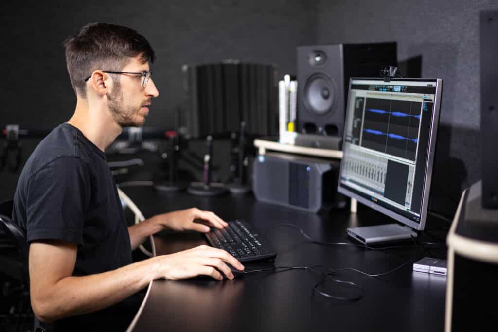 A man sits at the Recording Studio work station, where he is editing an audio file.