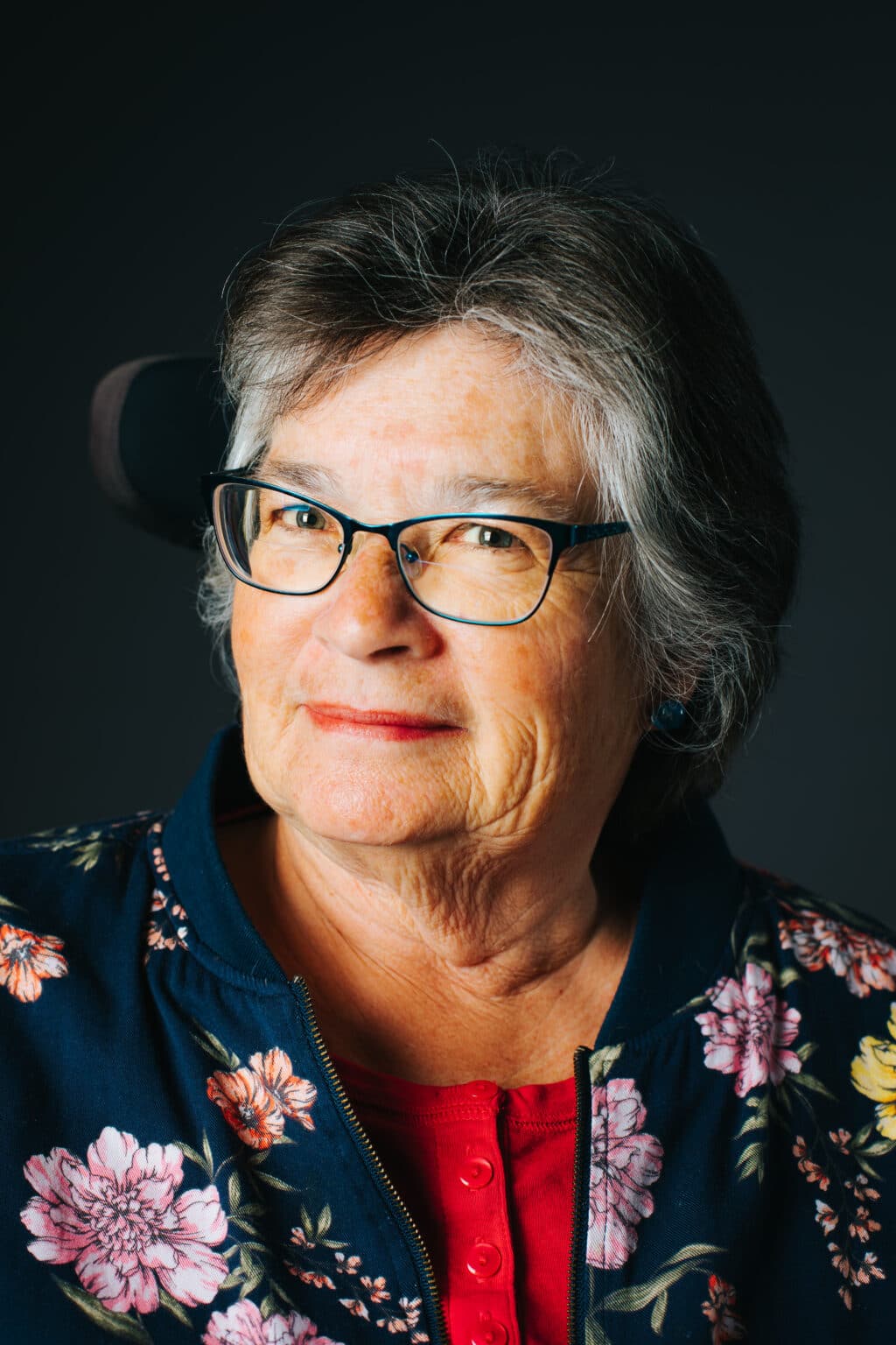 Headshot of Author Sandra Gail Lambert. Her face is lit up and turned a little to the left. She smiles slightly. She wears a red t-shirt and a navy jacket with large, colorful flowers.