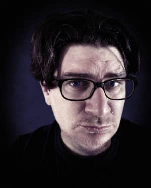 Author Andrew Shaffer, a white man with black hair and blue eyes. He is wearing black glasses and a humorous expression.