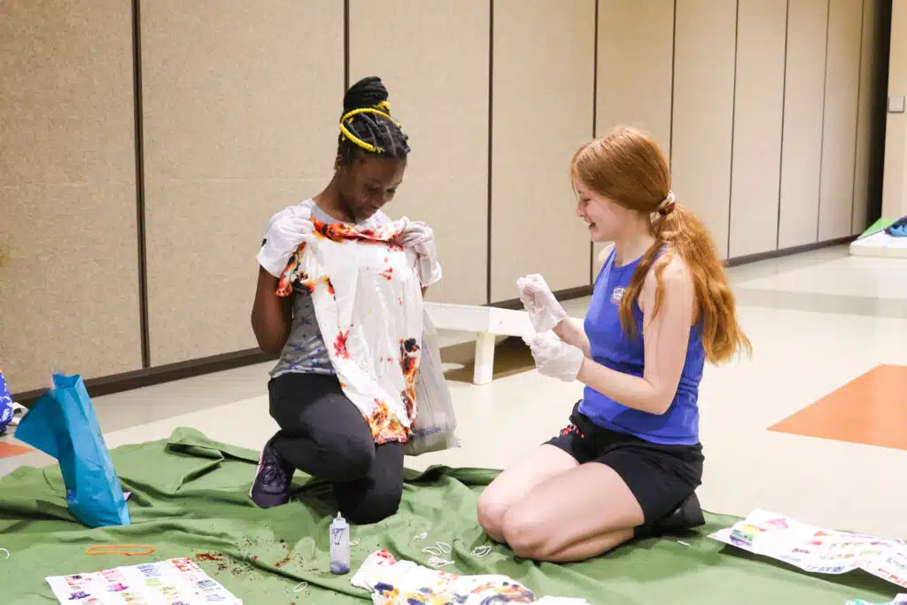 Two teen girls tie dye a t-shirt at the library.