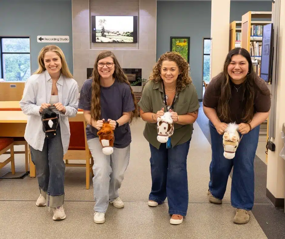 Four library staff members on stick horses line up for a race.